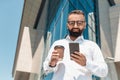 Happy mature businessman texting on cellphone and drinking takeout coffee, walking outside office building, empty space Royalty Free Stock Photo