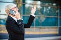 Happy mature businesswoman talking on the phone and gesturing with her hand, walking in front of an office building Royalty Free Stock Photo