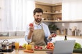 Happy mature caucasian male with beard in apron has video call, makes video holds tomato with hands Royalty Free Stock Photo