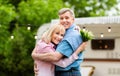 Happy mature couple with bouquet of field flowers hugging near trailer outdoors Royalty Free Stock Photo