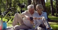 Happy mature couple relaxing in park on picnic using smartphone together Royalty Free Stock Photo