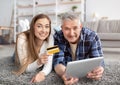Happy mature couple shopping online with tablet pc and credit card, lying on floor at home Royalty Free Stock Photo