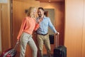 happy mature couple with suitcases laughing in hotel
