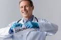 Happy and mature doctor in latex gloves tearing paper with coronavirus lettering