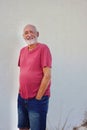 Happy mature elderly man wearing pink shirt and standing against white wall Royalty Free Stock Photo