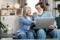 Happy mature family in casual outfit sitting together on couch and using wireless laptop. Royalty Free Stock Photo