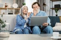 Happy mature family in casual outfit sitting together on couch and using wireless laptop. Royalty Free Stock Photo