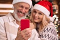 Happy mature family couple in santa hats using cell phone on Christmas. Royalty Free Stock Photo