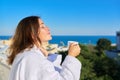 Happy mature female in white bathrobe on balcony of hotel in seaside resort town Royalty Free Stock Photo