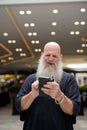 Happy mature handsome bald bearded man using phone in the city outdoors Royalty Free Stock Photo