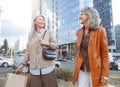 Happy mature ladies with shopping bags walk along modern city street