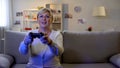 Happy mature lady playing video game on console, sitting home on sofa, leisure Royalty Free Stock Photo