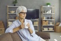Happy mature lady relaxing on sofa, enjoying good cup of tea, looking away and thinking Royalty Free Stock Photo
