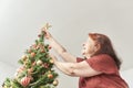 Happy woman smiling as she puts a gold star on the top of a Christmas tree Royalty Free Stock Photo