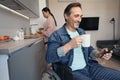 Smiling male using wheelchair and smartphone in kitchen with wife