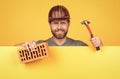 happy mature man bricklayer behind yellow paper for copy space hold hammer and brick, may 1.