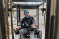 Happy mature man fork lift truck driver lifting pallet in storage warehouse and looking at camera. Royalty Free Stock Photo