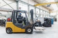 Happy mature man fork lift truck driver lifting pallet in storage warehouse and looking at camera.