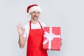 happy mature man in santa hat and red apron hold present. ok Royalty Free Stock Photo