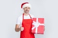 happy mature man in santa hat and red apron hold present. thumb up Royalty Free Stock Photo