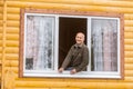 Happy mature man sitting on the window of a new wooden country house Royalty Free Stock Photo