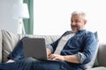 Happy mature man using laptop while resting on sofa Royalty Free Stock Photo