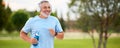 Happy mature man wearing headphones with water bottle in hand jogging outside in city park Royalty Free Stock Photo