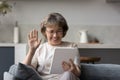 Happy mature 60s woman waving hand hello at tablet screen Royalty Free Stock Photo