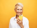 Happy mature senior woman with short hair holding smartphone using mobile online apps over yellow background Royalty Free Stock Photo