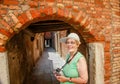 Happy mature tourist woman stays against narrow street in Venice