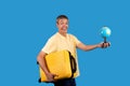 Happy mature traveler holding globe and travel suitcase, studio shot