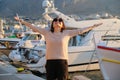 Happy mature woman with hands raised up standing on pier with boats