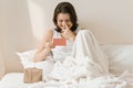 Happy mature woman at home in bed with surprise gift reading greeting card. Emotion of happiness, joy, surprise