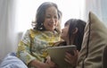 Happy mature woman with little granddaughter using digital tablet together, sitting on cozy couch in living room Royalty Free Stock Photo