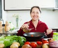 Happy mature woman pouring oil into fryingpan Royalty Free Stock Photo