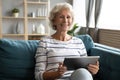 Happy mature woman sit on sofa using pad Royalty Free Stock Photo