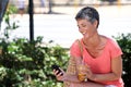 Happy mature woman sitting outdoors with drink and using mobile phone Royalty Free Stock Photo