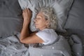 Happy mature woman sleeping on soft pillow under blanket.