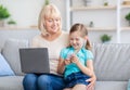 Happy mature woman using laptop hugging girl with smartphone Royalty Free Stock Photo