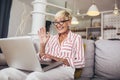 Mature woman waving to someone while having a video call over laptop at home Royalty Free Stock Photo