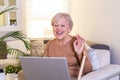 Happy mature woman waving to someone while having a video call over laptop at home. Gray-haired senior woman waving hand in front Royalty Free Stock Photo