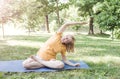 A happy mature woman in a yellow T-shirt is doing yoga sitting in the park in the lotus position doing sideways bends Royalty Free Stock Photo