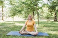 A happy mature woman in a yellow T-shirt is doing yoga sitting in the park in the lotus position doing sideways bends Royalty Free Stock Photo