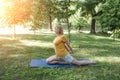 A happy mature woman in a yellow T-shirt is doing yoga sitting in the park in the lotus position doing sideways bends Royalty Free Stock Photo