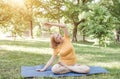 A happy mature woman in a yellow T-shirt is doing yoga sitting in the park in the lotus position doing sideways bends Royalty Free Stock Photo