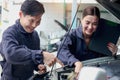 Happy mechanic man and woman mechanic in uniform discussing while working together with engine vehicle at garage, two auto Royalty Free Stock Photo