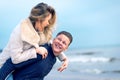 Happy man giving piggyback ride to his woman and laughing at beach. Smiling guy in love carrying on back her girlfriend Royalty Free Stock Photo