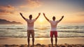 Happy male travelers raising arms up enjoying sunrise on the beach