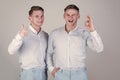 Happy men together. Two brothers showing thumbs up and ok gestures. Models winking and smiling on grey background. Twins Royalty Free Stock Photo