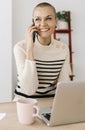 Happy mid adult woman talking on mobile phone sitting at office workplace Royalty Free Stock Photo